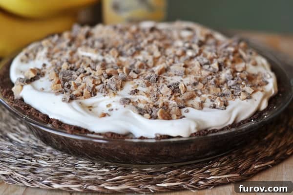 A stunning full view of the chocolate cookie crust banana pie, generously topped with whipped cream and chopped toffee, making it a feast for the eyes and the palate.