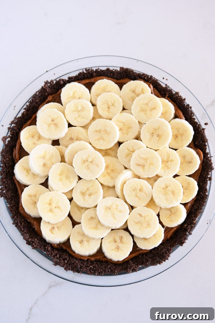 Perfectly sliced fresh bananas neatly layered over the smooth dulce de leche within the chocolate cookie crust, forming a beautiful foundation for the cream.