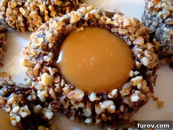Close-up top view of a chocolate turtle cookie, showcasing the glossy caramel filling nestled within the dark chocolate dough, surrounded by chopped pecans.