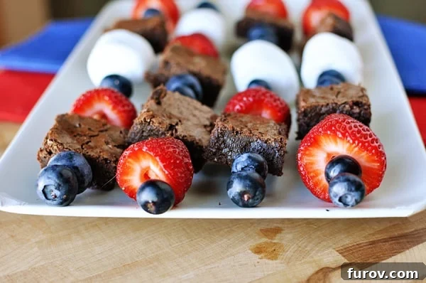 White platter with four brownie, marshmallow, and fruit kebabs laying side by side.
