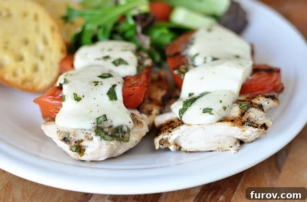 Grilled caprese chicken breasts arranged beautifully on a white platter, accompanied by a fresh side salad and golden garlic bread slices.