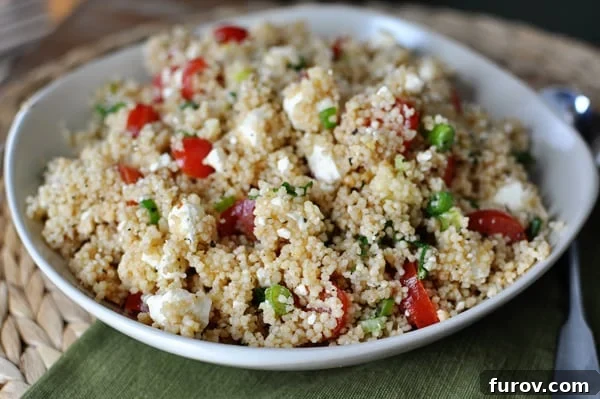 Vibrant Summer Couscous Salad 3 A closer view of the summer couscous salad in a white bowl, showing the fluffy texture of the couscous mixed with crumbled feta, halved cherry tomatoes, and green herbs.