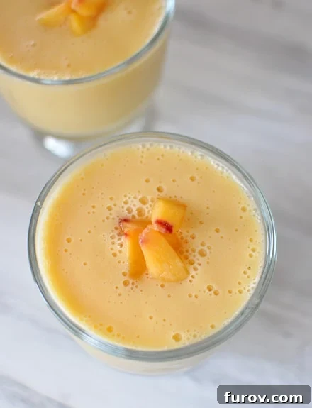 Close-up top view of a peach-orange smoothie in a glass goblet, garnished with small peach dices.