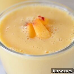 A tall glass of Peach-Orange Smoothie with a straw and a peach slice garnish.