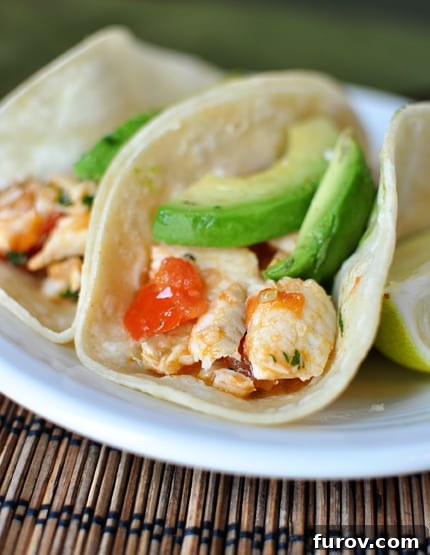 Close-up of perfectly assembled corn tortilla fish tacos, generously topped with vibrant diced tomatoes, creamy sliced avocados, and a sprinkle of fresh cilantro.