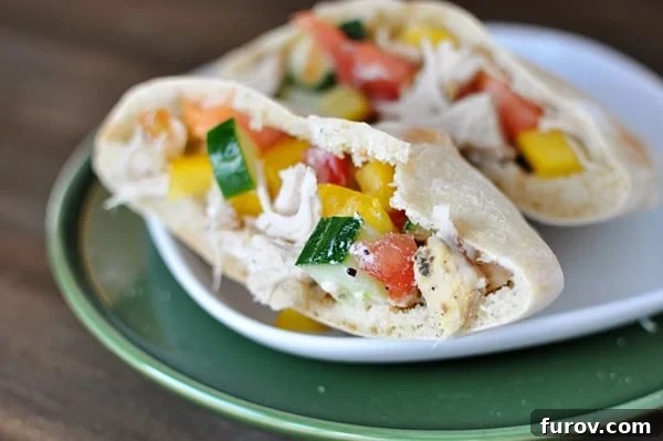 A pita cut in half on a white plate stuffed with a Greek chicken mixture.