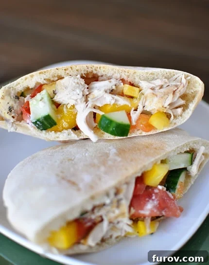 A pita cut in half with an inside view of a Greek chicken mixture stuffed inside each pita half.