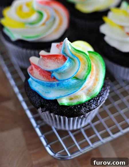Top view of chocolate cupcakes with vibrant tie-dye frosting on a cooling rack, showcasing a beautiful swirl of colors.