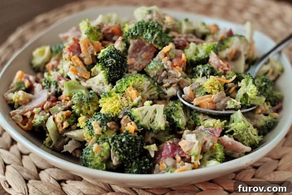 Ultimate Broccoli Salad 2 A large, inviting bowl filled to the brim with vibrant homemade broccoli salad, featuring a serving spoon resting inside, ready to be enjoyed.