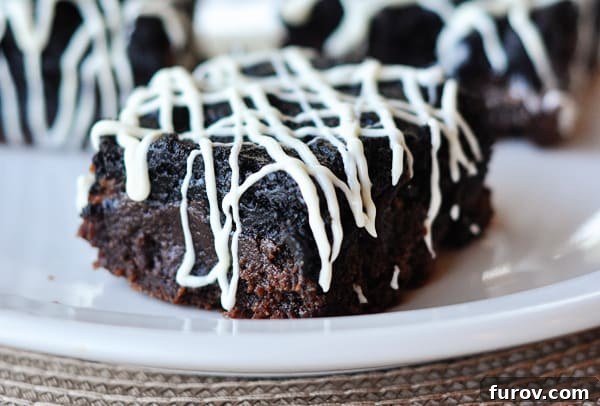 A single slice of Oreo truffle brownie with white chocolate drizzle on a white plate, showcasing its layers.