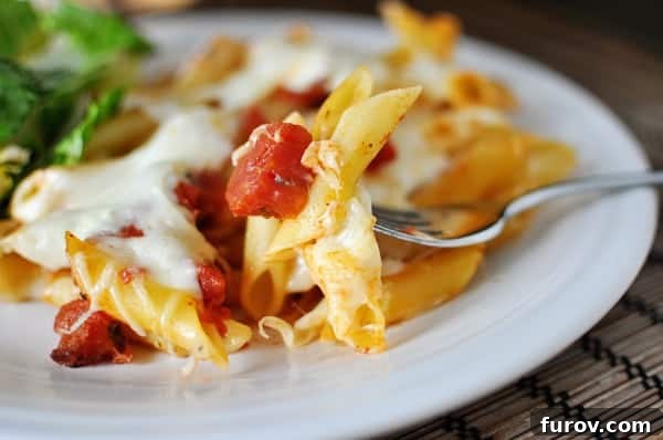 White plate with baked cheesy pasta and tomato dices, ready to be enjoyed.