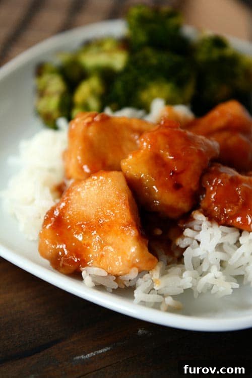 Bourbon sauce covered chicken on white rice on a white plate, garnished with green onions.