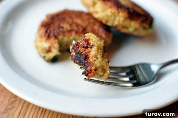 White plate showcasing golden-brown cooked quinoa patties, with a fork taking a satisfying bite.