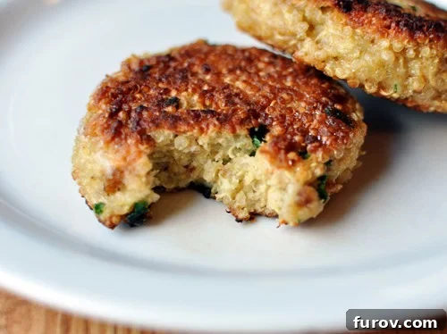 A single golden-brown cooked quinoa patty on a white plate with a small bite taken out, revealing its hearty interior.