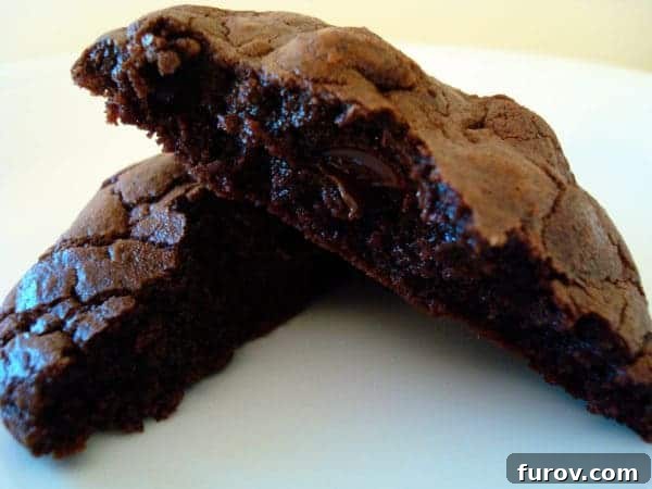 Double Chocolate Fudge Cookies 2 A perfectly baked, thick double chocolate cookie split in half, revealing its chewy interior and melted chocolate chunks, resting on a pristine white plate.