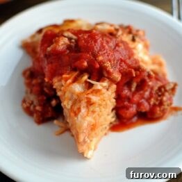 A triangle shaped serving of cooked spaghetti pie topped with red spaghetti sauce.