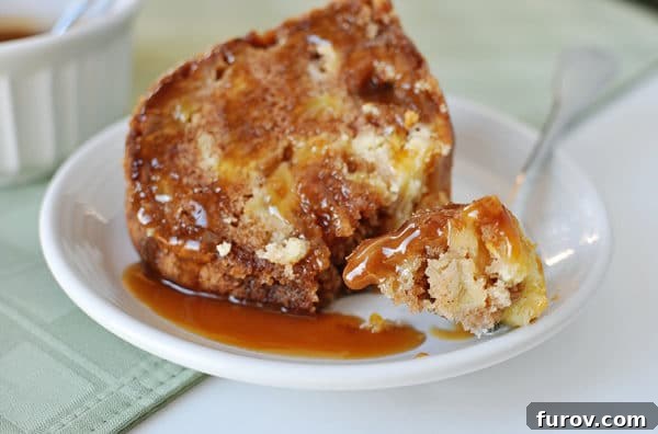 Close-up of a caramel apple bundt cake slice on a white plate with a bite taken, revealing the cream cheese swirl and apple pieces.