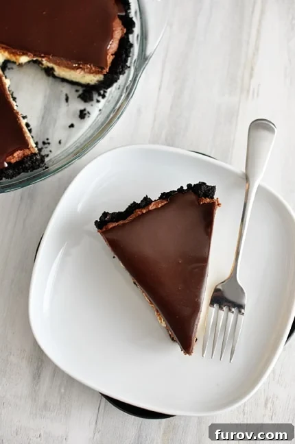A delectable slice of chocolate mousse cheesecake pie with a rich cookie crust and a glossy chocolate ganache topping, served on a pristine white plate.
