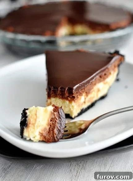 A close-up of a slice of chocolate mousse cheesecake pie, with a bite taken out, revealing its luscious layers of crust, cheesecake, mousse, and ganache, presented on a white plate.