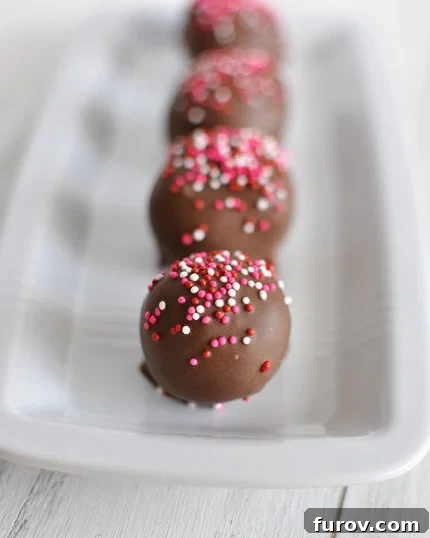 A rectangular white dish filled with perfectly formed brownie truffles, some topped with colorful sprinkles, others plain chocolate.