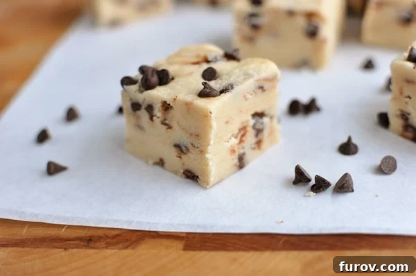 Perfectly cut squares of rich chocolate chip cookie dough fudge, garnished with mini chocolate chips, arranged beautifully on a sheet of parchment paper.