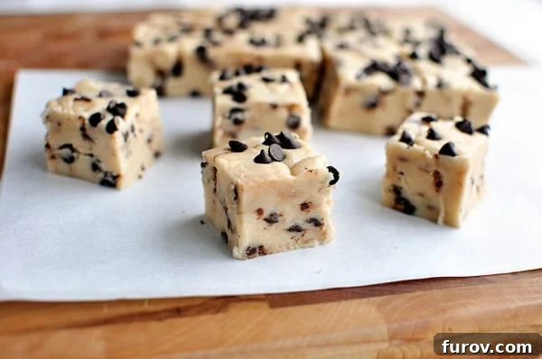 A large rectangular slab of freshly made chocolate chip cookie dough fudge being carefully sliced into smaller, uniform squares on a sheet of parchment paper.