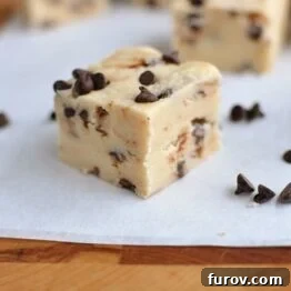 A close-up of several small squares of chocolate chip cookie dough fudge, garnished with extra mini chocolate chips, highlighting its soft texture.
