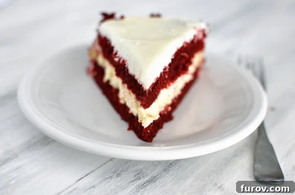 Decadent Red Velvet Cheesecake 2 A slice of elegant red velvet cheesecake cake showing distinct layers of cake and cheesecake, topped with cream cheese frosting.