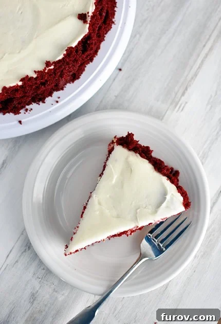 Decadent Red Velvet Cheesecake 3 An overhead view of a beautifully frosted slice of red velvet cheesecake cake on a white plate, showcasing the frosting swirls and cake crumbs.