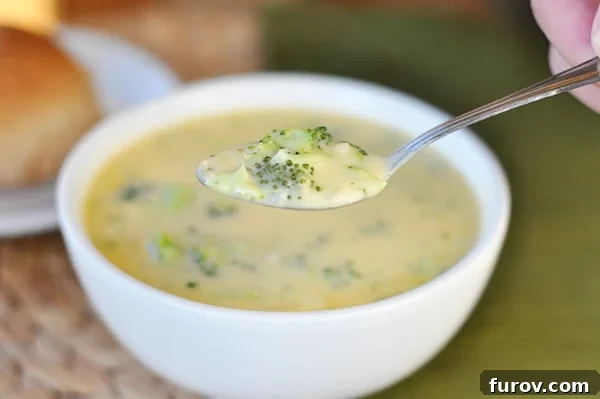 A close-up of a white bowl of homemade broccoli cheese soup, with a spoon scooping out a creamy bite, highlighting its rich texture.