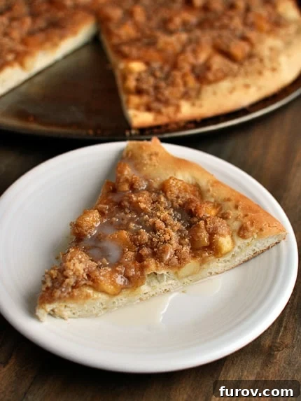 Golden Apple Streusel Dessert Pizza 2 A perfectly baked slice of apple cinnamon streusel dessert pizza resting in front of the full pizza, showcasing the layers of crust, apple, and streusel.