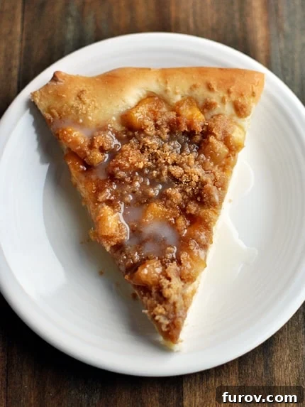 Golden Apple Streusel Dessert Pizza 3 Top-down view of a single slice of apple cinnamon dessert pizza on a clean white plate, emphasizing the golden streusel and creamy glaze.