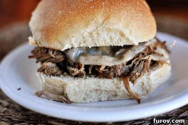 Melt-in-Your-Mouth Slow Cooker Italian Beef 9 A delicious Italian beef sandwich served on a white plate, ready to be enjoyed.