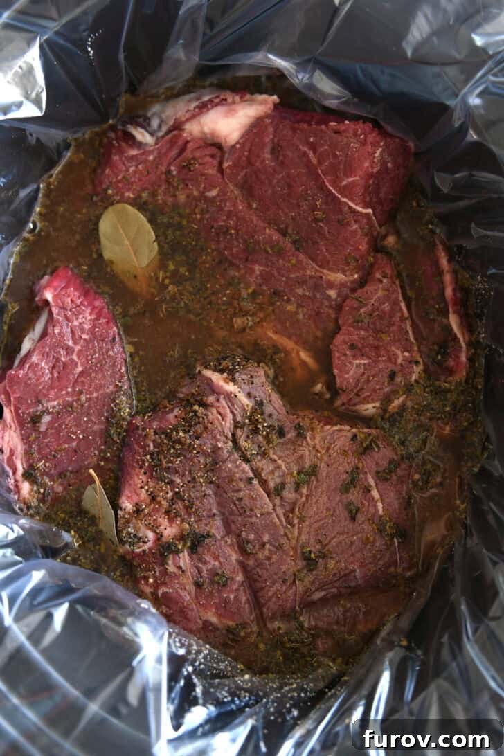 Melt-in-Your-Mouth Slow Cooker Italian Beef 4 Black slow cooker pot lined with a slow cooker liner, containing a chuck roast, bay leaves, and beef broth mixture before cooking.