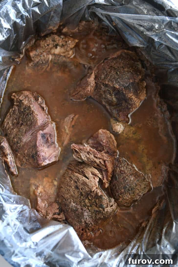 Melt-in-Your-Mouth Slow Cooker Italian Beef 5 Black slow cooker insert with slow cooker liner filled with perfectly cooked, tender beef and rich beef broth mixture.