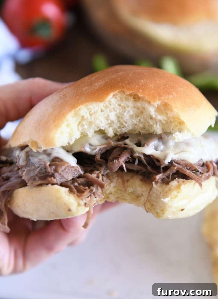 Melt-in-Your-Mouth Slow Cooker Italian Beef 7 Slow cooker Italian beef on a golden crusty roll with melted provolone cheese, a perfect bite taken, held by a hand.