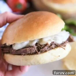 Melt-in-Your-Mouth Slow Cooker Italian Beef 8 Slow cooker Italian beef on crusty rolls with provolone cheese and one bite taken out; hand holding sandwich.
