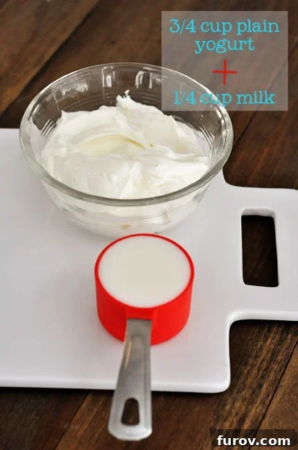 A white cutting board showcasing a bowl of plain yogurt and a measuring cup filled with milk, ingredients for a yogurt-based buttermilk substitute.