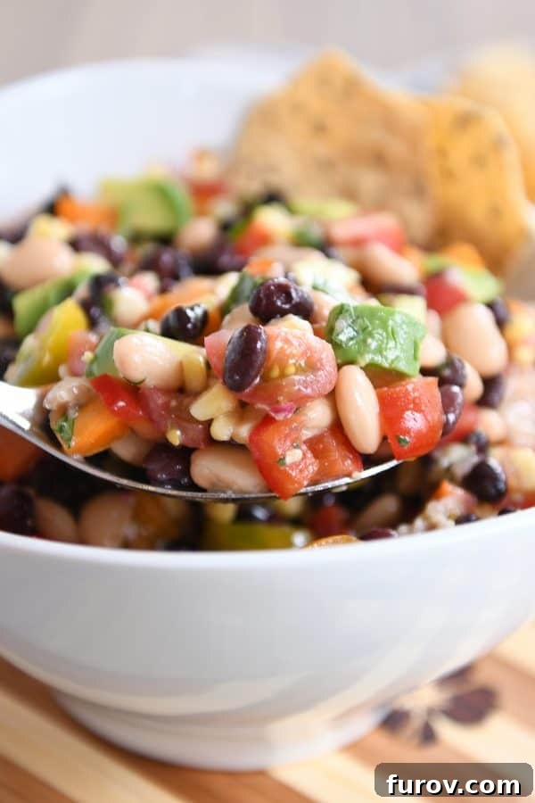 Zesty Cowboy Caviar Explosion 3 A metal spoon scooping a generous portion of colorful cowboy caviar dip from a white bowl, showcasing its rich texture.