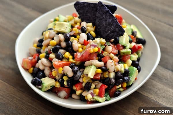 Zesty Cowboy Caviar Explosion 7 A beautiful white bowl brimming with a colorful bean, corn, and avocado dip, ready for a gathering.