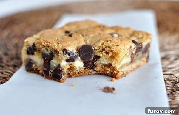 A delicious cheesecake filled chocolate chip bar with a bite taken out, resting on a white piece of parchment paper.