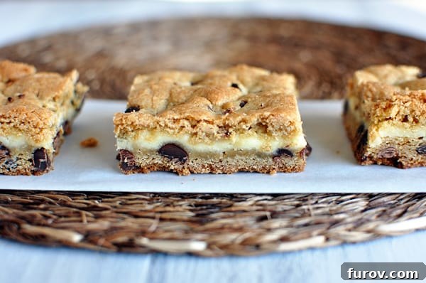Three perfectly crafted chocolate chip bars with a decadent cheesecake middle, neatly arranged on a sheet of parchment paper.