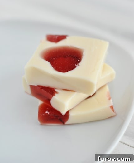 Three squares of white Jello with red Jello hearts inside on a white plate stacked on top of each other.