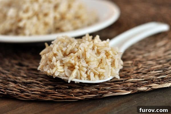 A spoonful of perfectly cooked brown rice, showing individual, fluffy grains, with a pot of rice in the background.