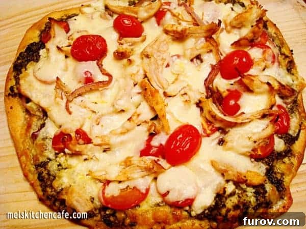 Delicious pesto pizza topped with shredded chicken, fresh tomatoes, and melting feta cheese, ready to be served.