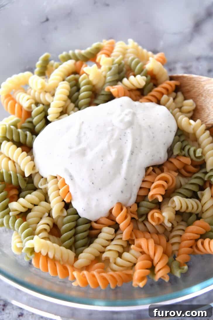 Vibrant Tricolor Pasta Medley 3 Dollop of caesar salad dressing on cooked pasta in glass bowl.