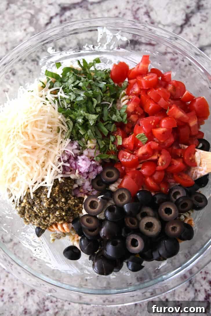 Vibrant Tricolor Pasta Medley 5 Top down view of olives, pesto, red onions, tomatoes, basil and parmesan cheese in glass bowl.