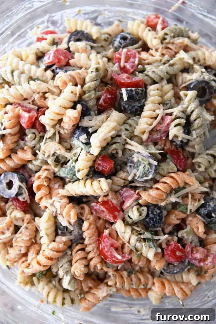 Vibrant Tricolor Pasta Medley 6 Top down view of tri-color rotini pasta in bowl with salad dressing, olives, tomatoes and parmesan cheese.
