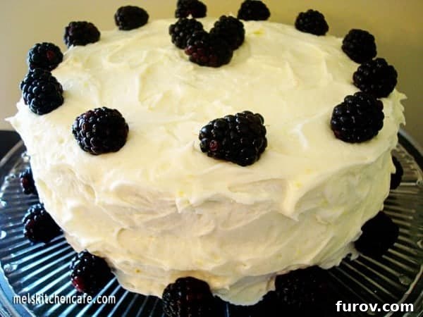 A beautifully frosted lemon cake adorned with fresh blackberries, ready to be sliced.
