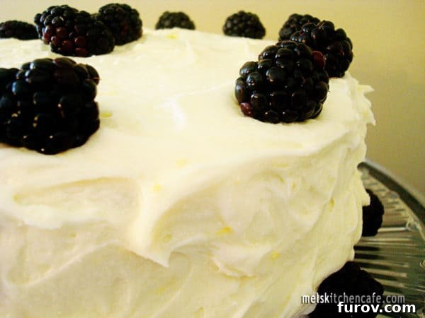 A close-up shot of the frosted lemon cake, topped with fresh blackberries, showcasing its inviting texture.